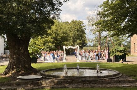 Hochzeit auf dem Hofplatz des Wittkielhofs. Im Vordergrund Bäume.