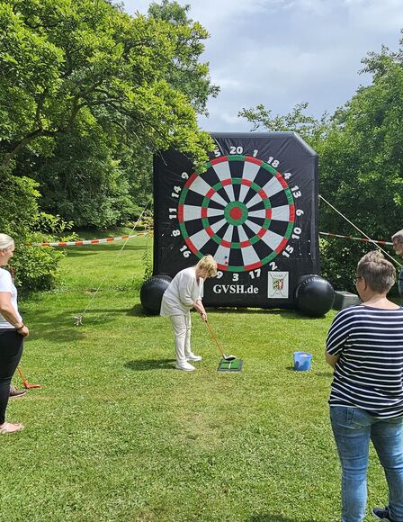 Vordergrund Personen, Bildmitte riesige Dartscheibe