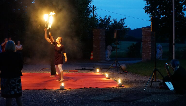 Links Vordergrund zwe Personen mit Fackeln auf rotem Ausleger. Feuertöpfe am Rand des Ausleger. LInker Bildrand Zuschauer. Hintergrund rechts Torpfosten Wittkielhof mit Löwen Staturen.