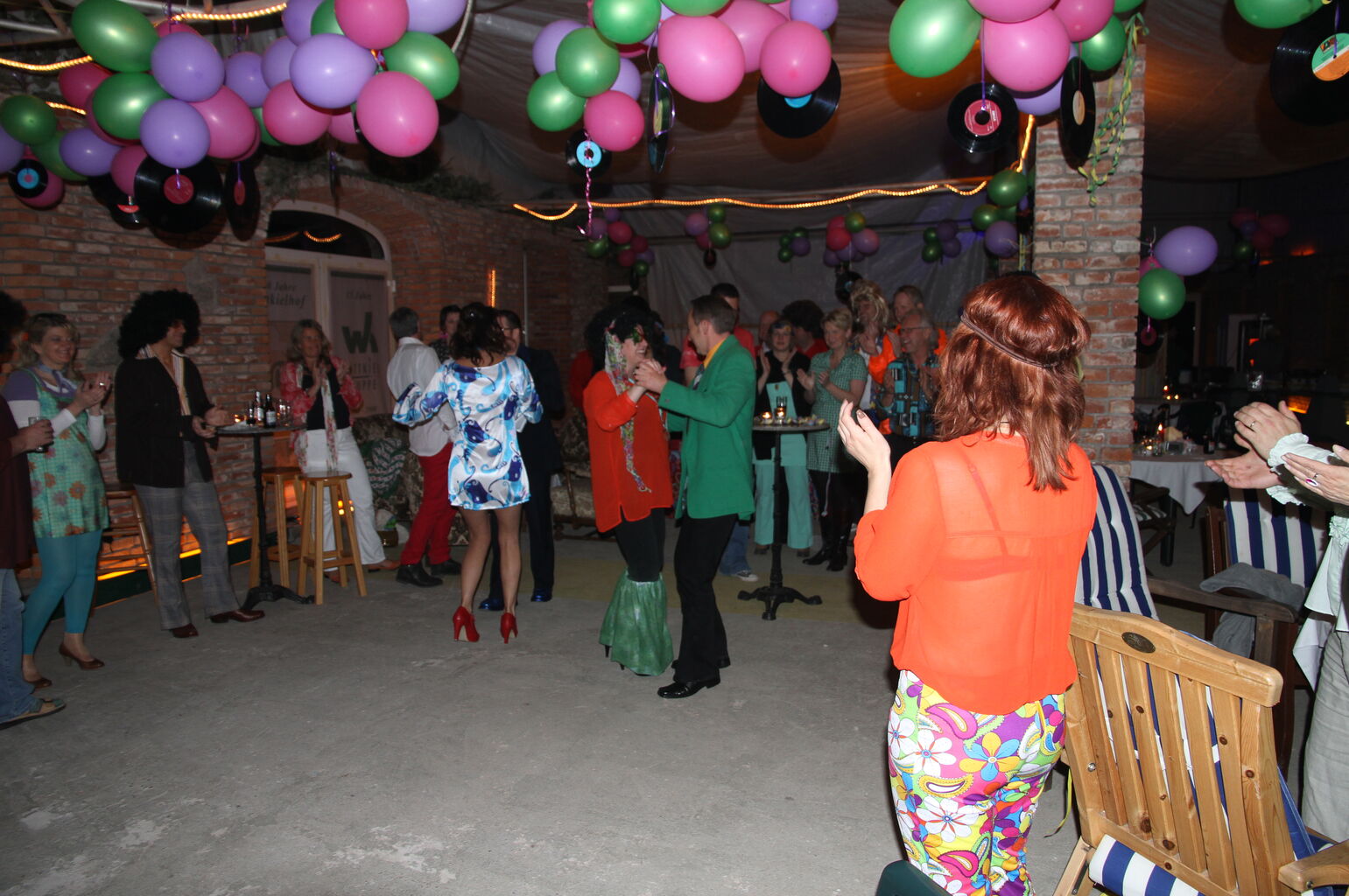 Mehrere Menschen feiern in einem Raum, unter der Decke schweben zahlreiche Luftballons.