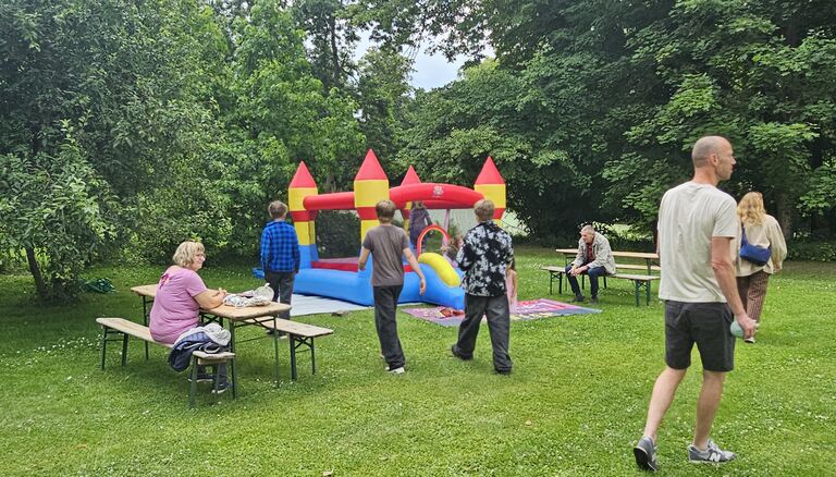 Hintergrund Blau-Gelb-Rote Hüpfburg auf Wiese, Vordergrund Kinder