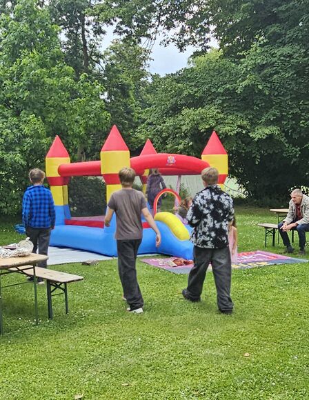 Hintergrund Blau-Gelb-Rote Hüpfburg auf Wiese, Vordergrund Kinder