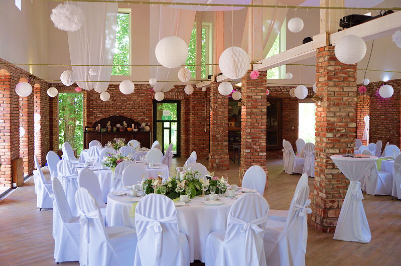 Eventscheune, Weitwinkel-Aufnahme. Dekorationen in Pink und viel Grün. Weiße Bezüge für Tische und Stühle.