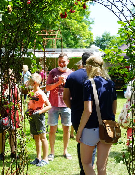 Metallbogen mit Kletterrosen, Zwei Personen laufen hindurch. Dahinter lächelnder Mann und Junge