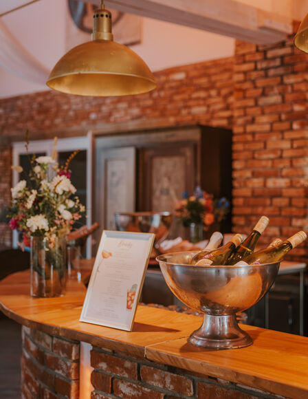 Bar-Tresen. Es stehen eine Schale mit gekühlten Weinflaschen und ein Bilderrahmen mit schwer-lesbarem Text oben drauf.