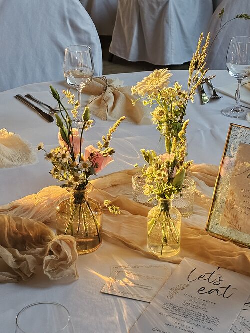 Nahaufnahme Tisch. Sträußchen mit weißen und rosanen Blumen. Tischdeko in Weiß udn Beige.