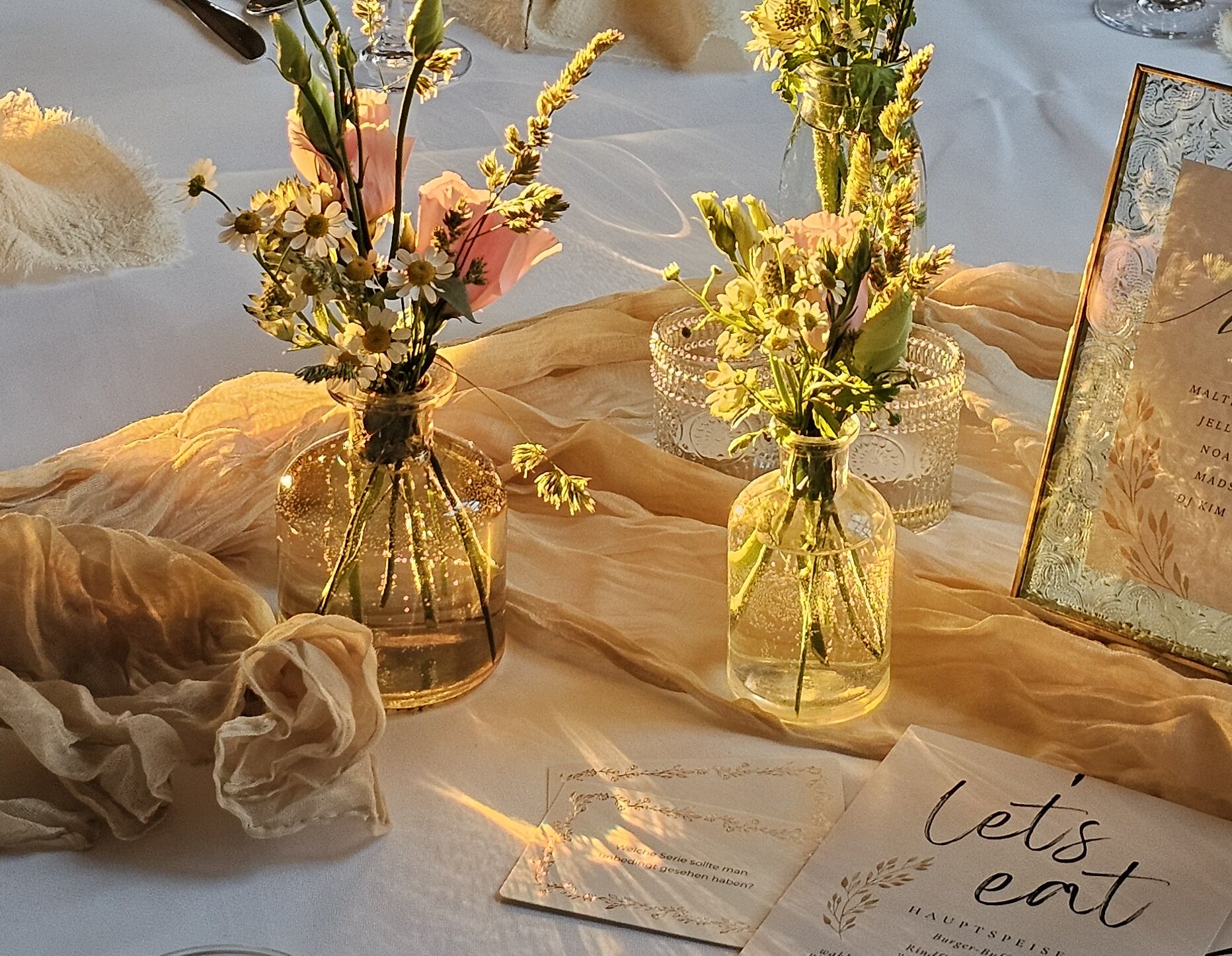 Nahaufnahme Tisch. Sträußchen mit weißen und rosanen Blumen. Tischdeko in Weiß udn Beige.