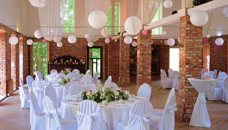 Eventscheune, Weitwinkel-Aufnahme. Dekorationen in Pink und viel Grün. Weiße Bezüge für Tische und Stühle.