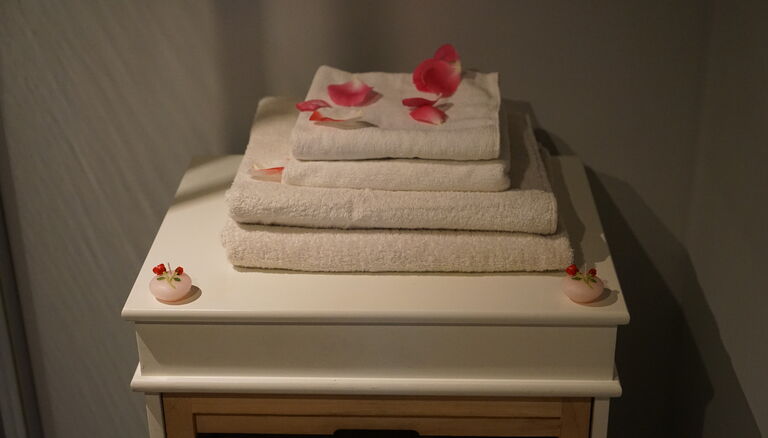 zwei Sets Handtücher aus großem und kleinem auf einem Tischchen. Zwei Seifen daneben. Dekoriert mit Rosenblättern