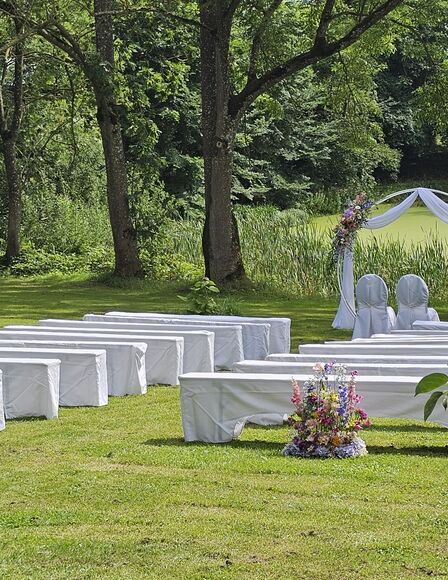 Hochzeitslocation auf Wiese. Bänke und Dekorationen stehen schon. Es sind noch keine Leute da.