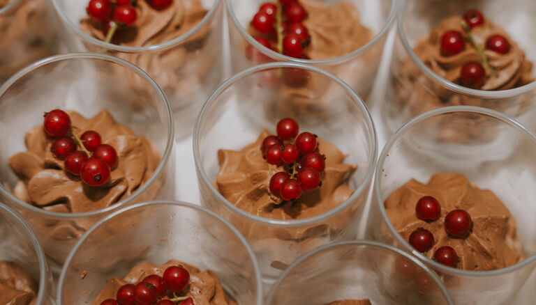 Gläser mit Schokoladencreme. Auf jedem Schokoladen-Häufchen liegen Johannisbeeren.