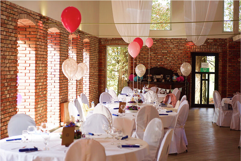 Eventscheune, Tischdekorationen. Tische mit Pinken Sträußen. Blaue Servietten. Rote, pinke und beigefarbene Luftballons.