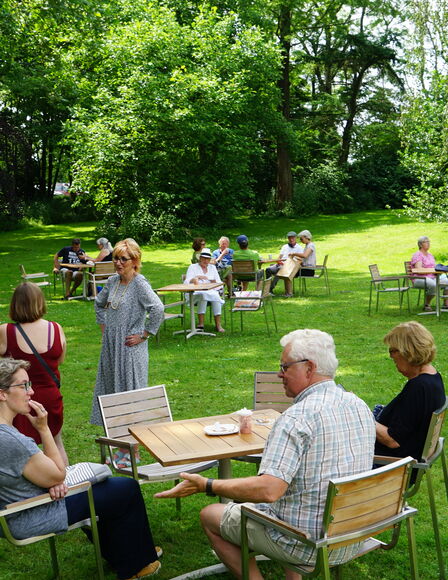 Sommermarkt, Wiese mit Tischen und Stühle, teilweise besetzt. Es sind zahlreiche Menschen auf dem Bild