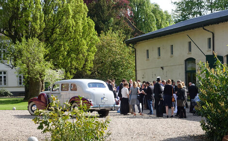 Hochzeitsgesellschaft und Oldtimer vor der Eventscheune Wittkielhof.