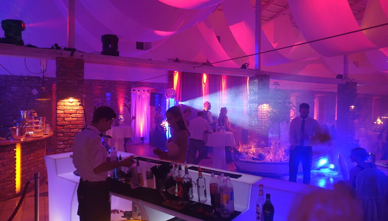 Bar samt Personal während einer Party in der Eventscheune. Licht ist Pink, Violett und Blau.