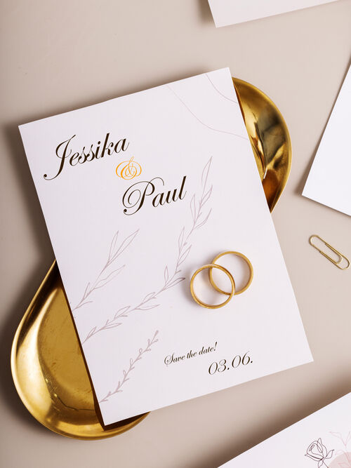 Eine Hochzeitseinladung zum dritten Juni. Es leigen zwei goldene Ringe auf der Karte.
