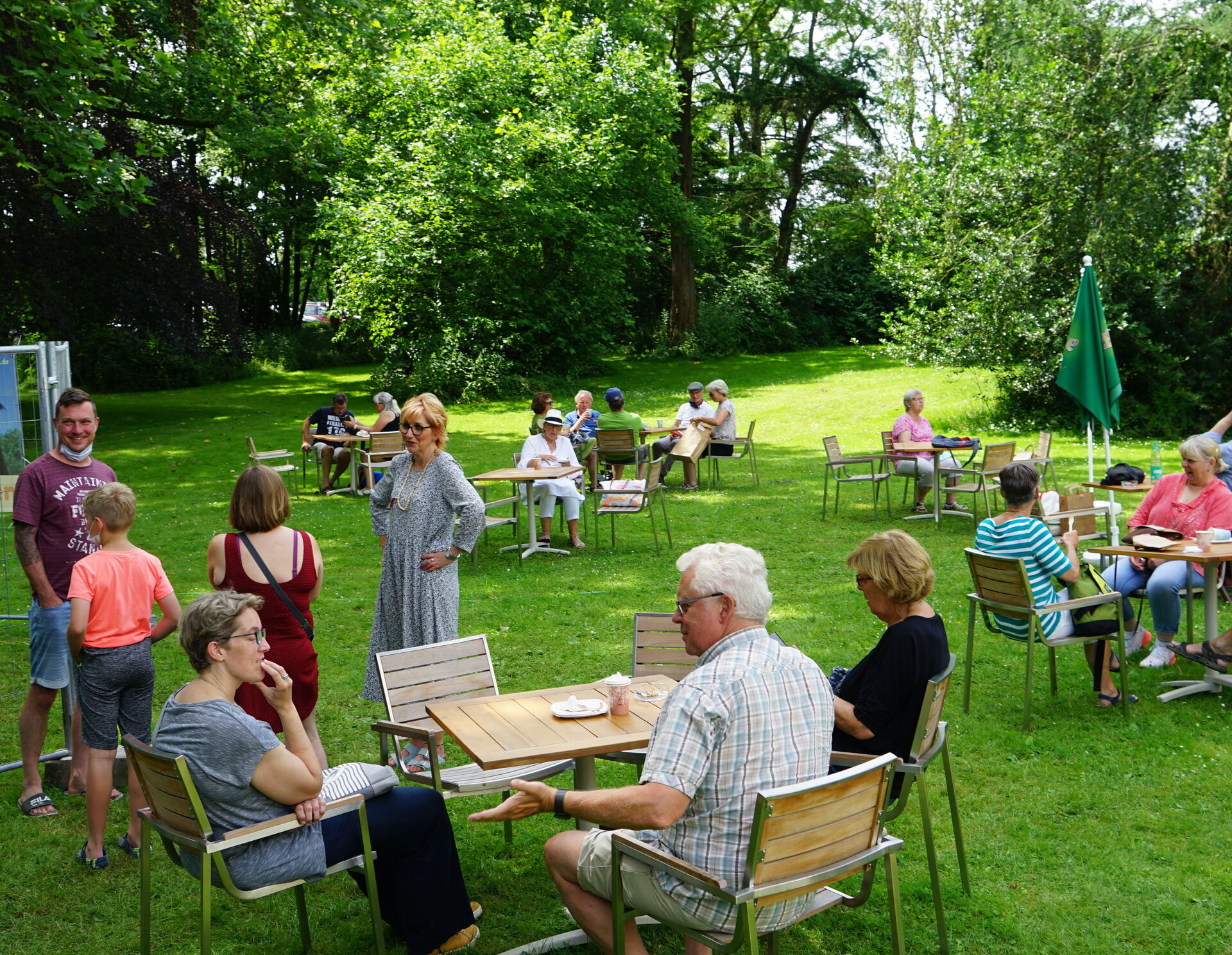 Sommermarkt, Wiese mit Tischen und Stühle, teilweise besetzt. Es sind zahlreiche Menschen auf dem Bild