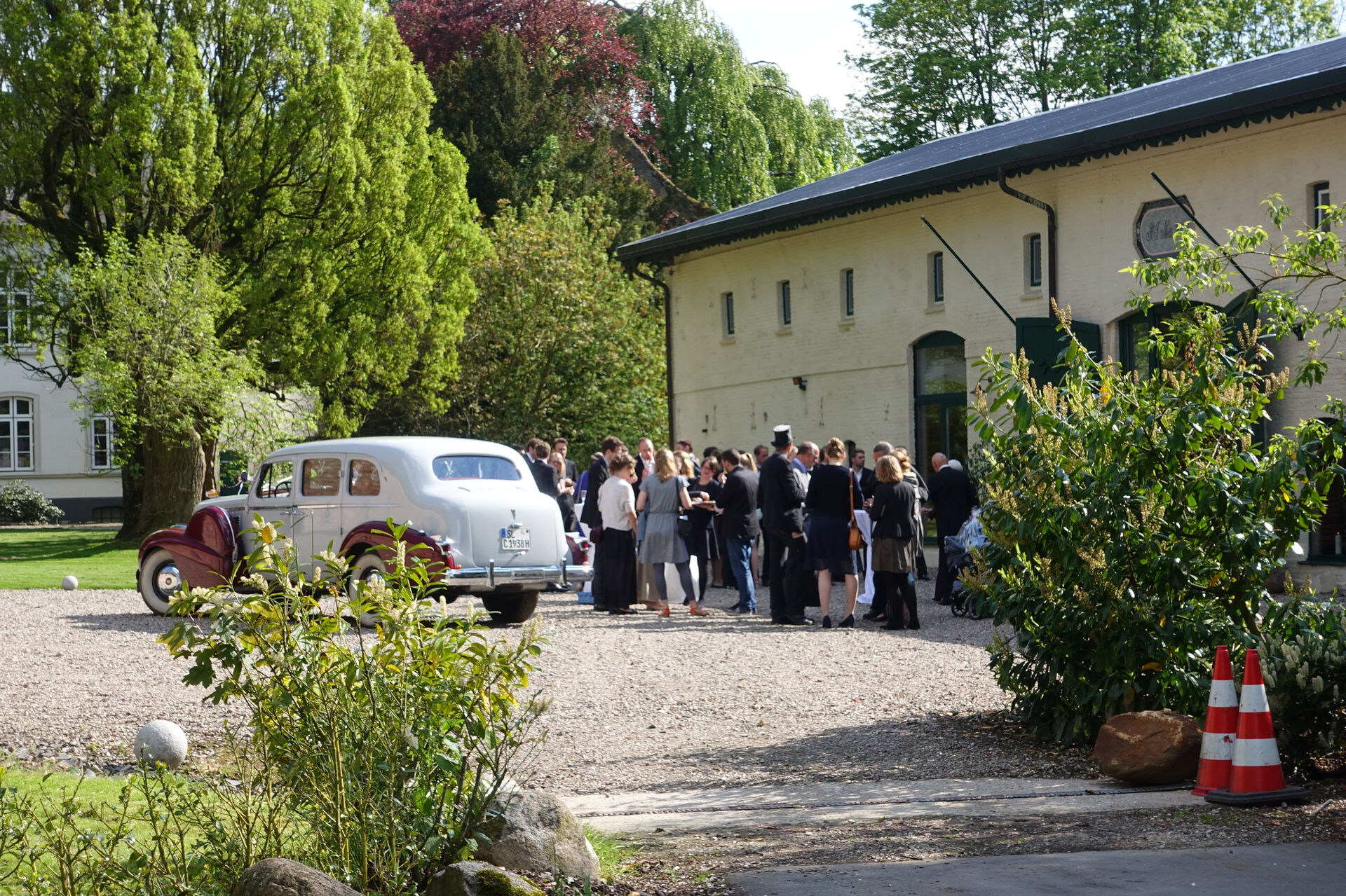 Hochzeitsgesellschaft und Oldtimer vor der Eventscheune Wittkielhof.
