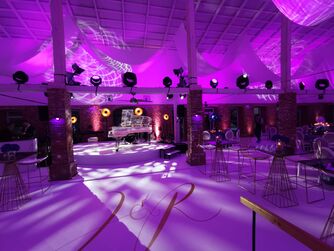 Bild von der Eventscheune. Im Vordergrund edle Tische und Stühle. Im Hintergrund ein gläserner Flügel.