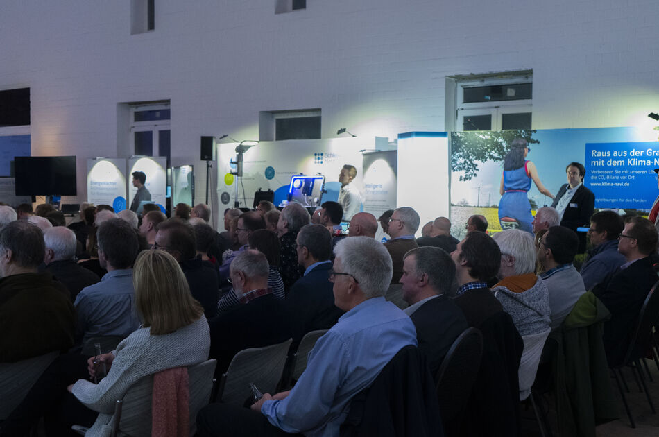 Präsentations-Stände vor einer Scheune, Sprecher und Gäste sind auf dem Bild, GFokus auf sitzende Gäste