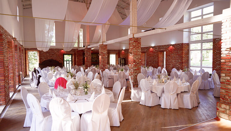 Eventscheune, Weitwinkel-Aufnahme. Dekorationen in Weiß und Pink. Weiße Bezüge auf Tischen und Stühlen..