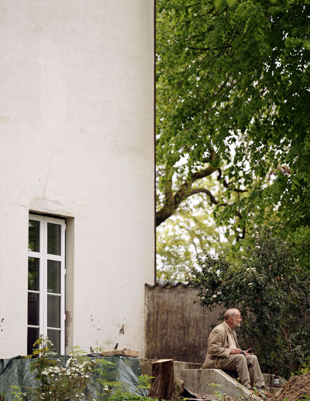 Links Gebäudewand mit halbfertiger Terasse, Rechts, ein älterer Herr auf halbfertiger Treppe