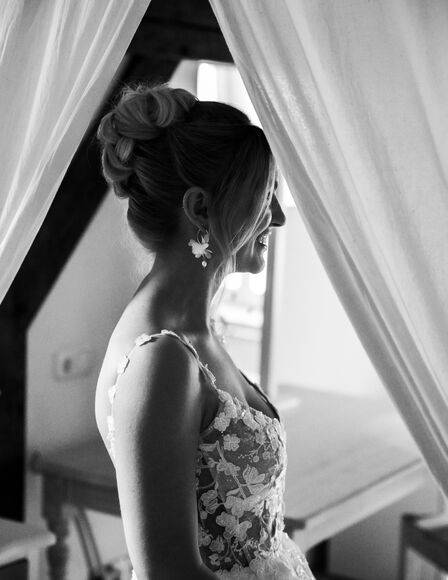 Bild schwarz-weiss, Braut steht vor Himmelbett in Hochtiedsstuuv, schaut nach rechts, lächelt