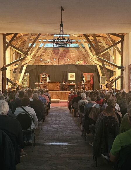 Asmus-Petersen Scheune, Hintergrund Bühne, Vordergrund und Bildmitte, Stuhlreihen gefüllt mit Menschen