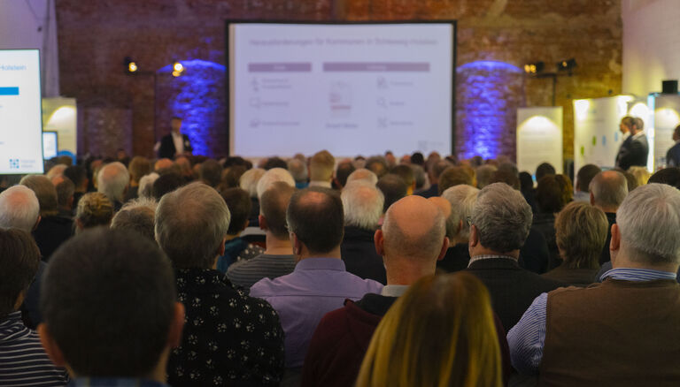 Eine Präsensation in der Eventscheune. Viele Menschen sehen sie sich an.