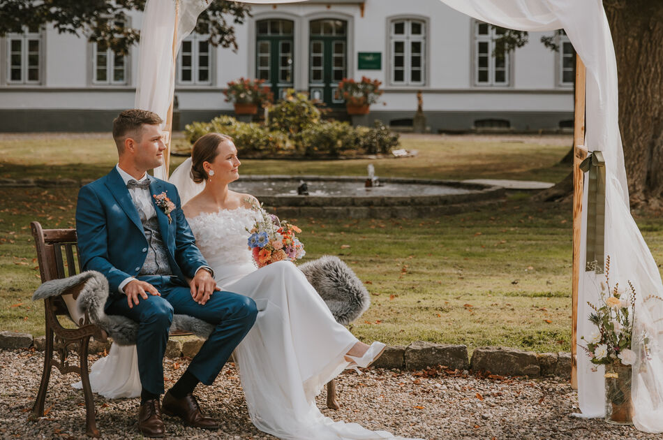 Hochzeitspaar vor mit Stoff bespanntem Bogen. Im Hintergrund Wittkielhof-Hauptgebäude, Aufnahme von weiter weg