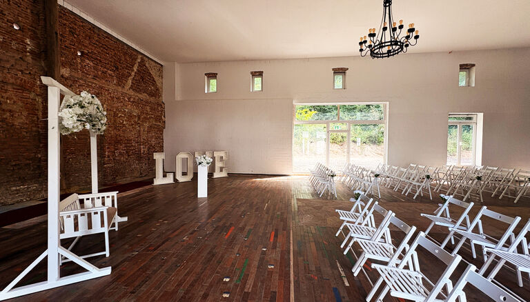Scheune für Hochzeit dekoriert, weiße Klappstühle, links vorne eine hübsche Bank