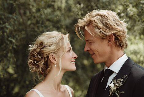 Hochzeitspaar sieht sich liebevoll in die Augen. Bäume im Hintergrund.