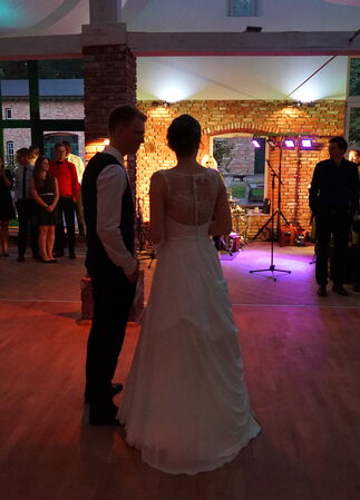 Hochzeitspaar in Eventscheune bei Dämmerung. Hochzeitsgesellschaft und -Band im Hintergrund.