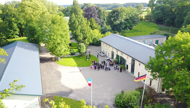 Drohnenaufnahme vom Wittkielhof. Eine Gesellschaft steht vor der Eventscheune.