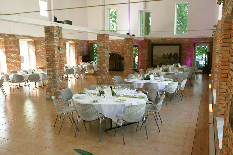 Eventscheune, Weitwinkel_Aufnahme. Dekorationen in Grün. Weiße Tischdecken. Stühle mit grünen Lehnen.