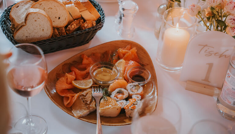 Buffet-Tisch. Vorne eine Schale mit Lachs und Sushi-Stücken. Hinten eine Schale mit verschiedenen Brotsorten.