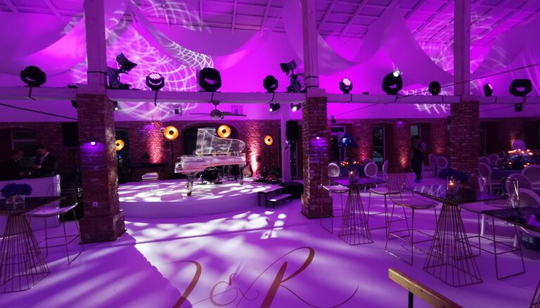 Bild von der Eventscheune. Im Vordergrund edle Tische und Stühle. Im Hintergrund ein gläserner Flügel.