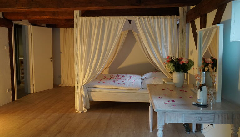 Hochtiedsstuuv, im Bild das Himmelbett, Tisch mit Champagner und Gläsern sowie offene Tür zum Badezimmer