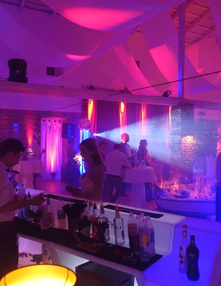 Bar samt Personal während einer Party in der Eventscheune. Licht ist Pink, Violett und Blau.