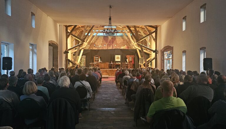 Asmus-Petersen Scheune während Veranstaltung. Zahlreiche Menschen sitzen auf Stühlen mit dem Rücken zur Kamera.
